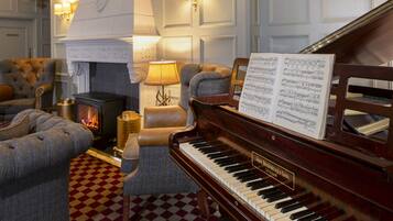 Een vleugelpiano met bladmuziek, een open haard, comfortabele fauteuils en een geruite vloer in een smaakvol ingerichte kamer.