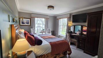 A hotel room with a bed, bedside table, lamp, TV, and a desk with a chair.