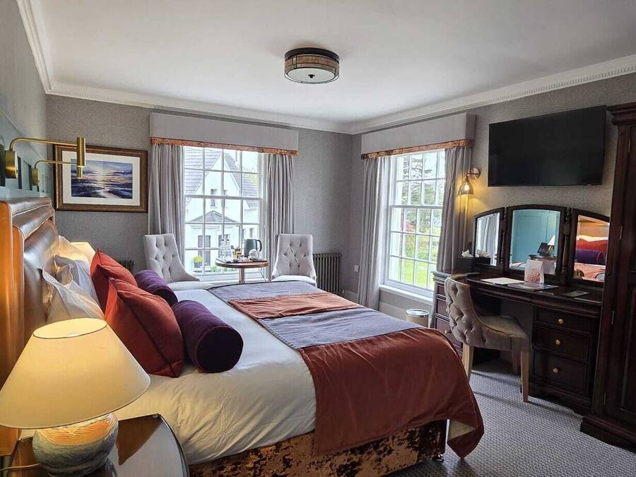 A hotel room with a bed, bedside table, lamp, TV, and a desk with a chair.