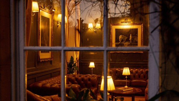 A warmly lit living room with a leather sofa, a coffee table, and wall-mounted lamps. - Knipoch House Hotel (Oban)
