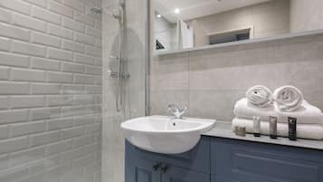 Un baño moderno con cabina de ducha de vidrio, lavamanos blanco y tocador con armarios azules.
