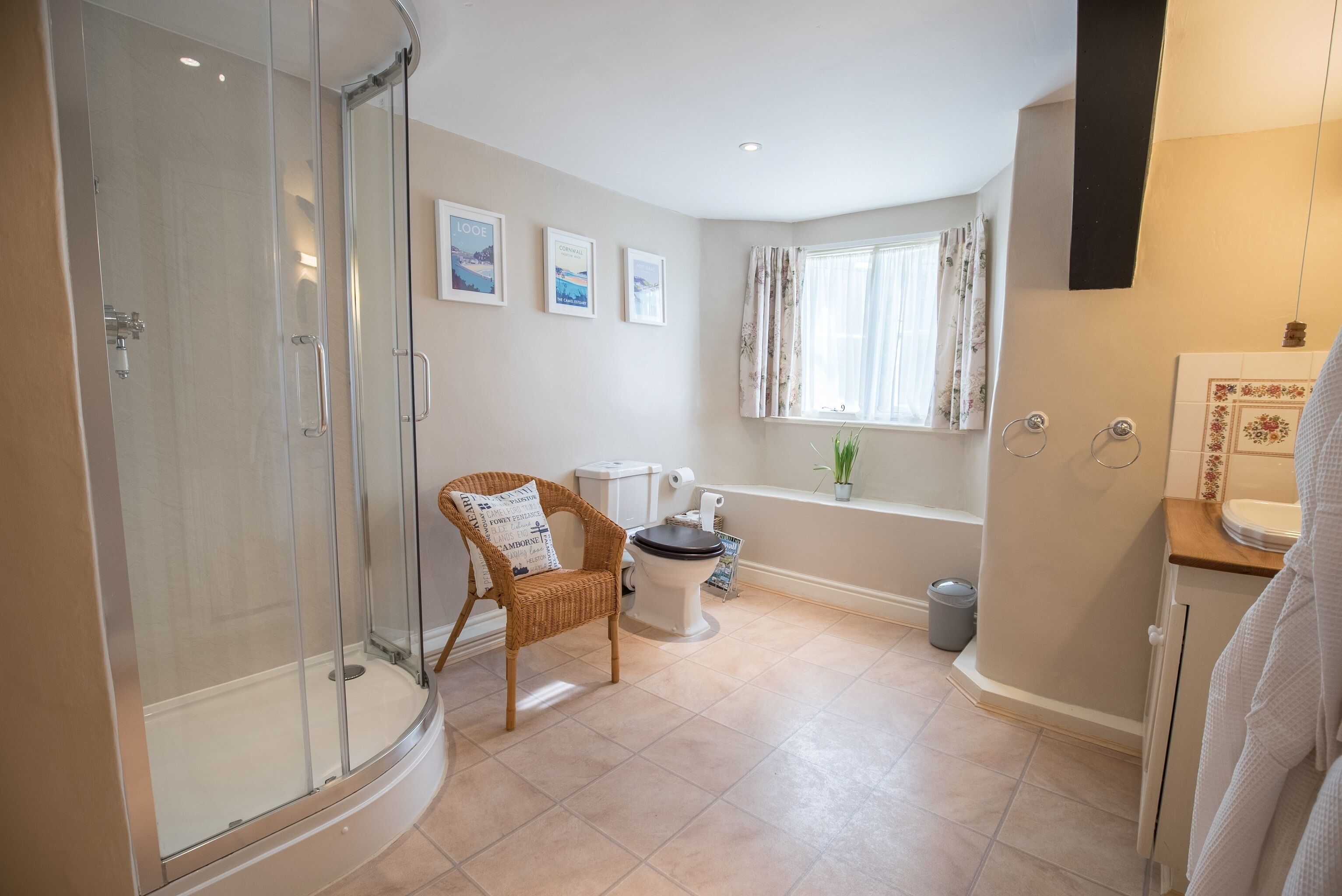 Une salle de bain avec une douche à parois de verre, des toilettes, une baignoire et un fauteuil en osier agrémenté d’un coussin.