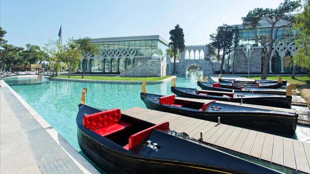 A swimming pool with boats and a stone bridge in the background. - Fairmont Baku - Flame Towers (Baku)