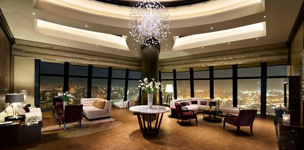 A luxurious hotel lobby with a large chandelier, plush seating, and a panoramic city view.