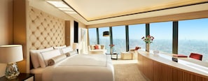 A hotel room with a large bed, a desk, a sofa, and a view of the city.