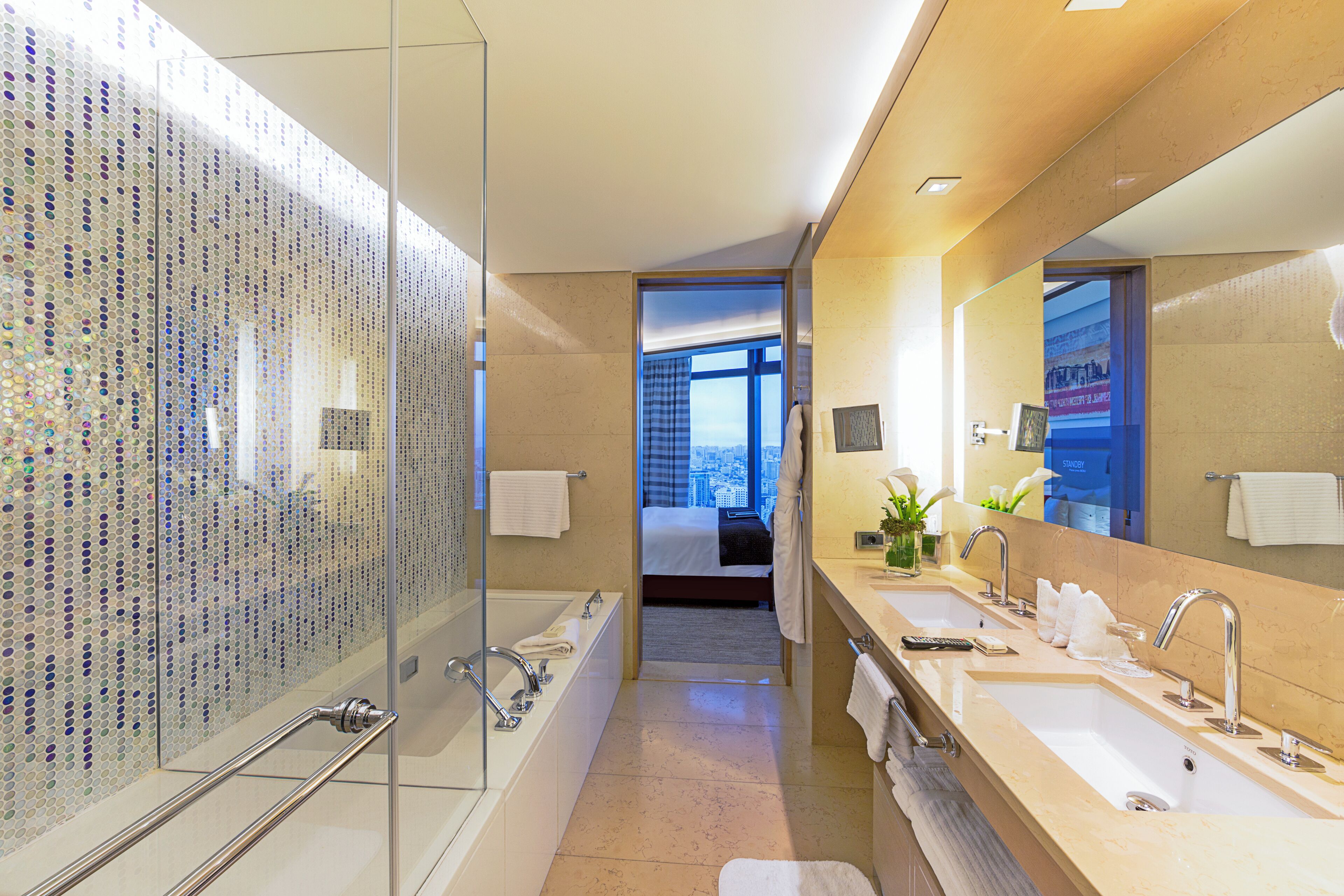 Ein modernes Hotelbad mit Glasdusche, zwei Waschbecken und einem großen Spiegel.