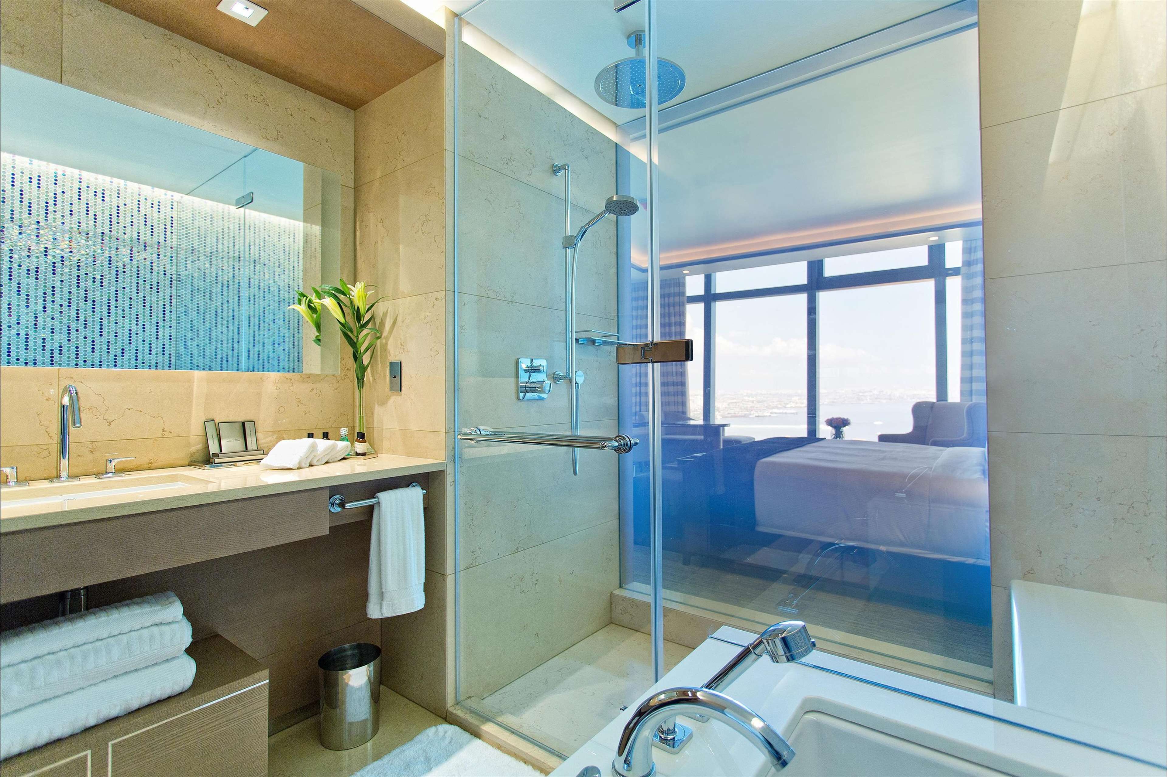 Une salle de bain moderne dotée d’une douche à parois de verre, d’un grand miroir et offrant une vue sur l’extérieur.