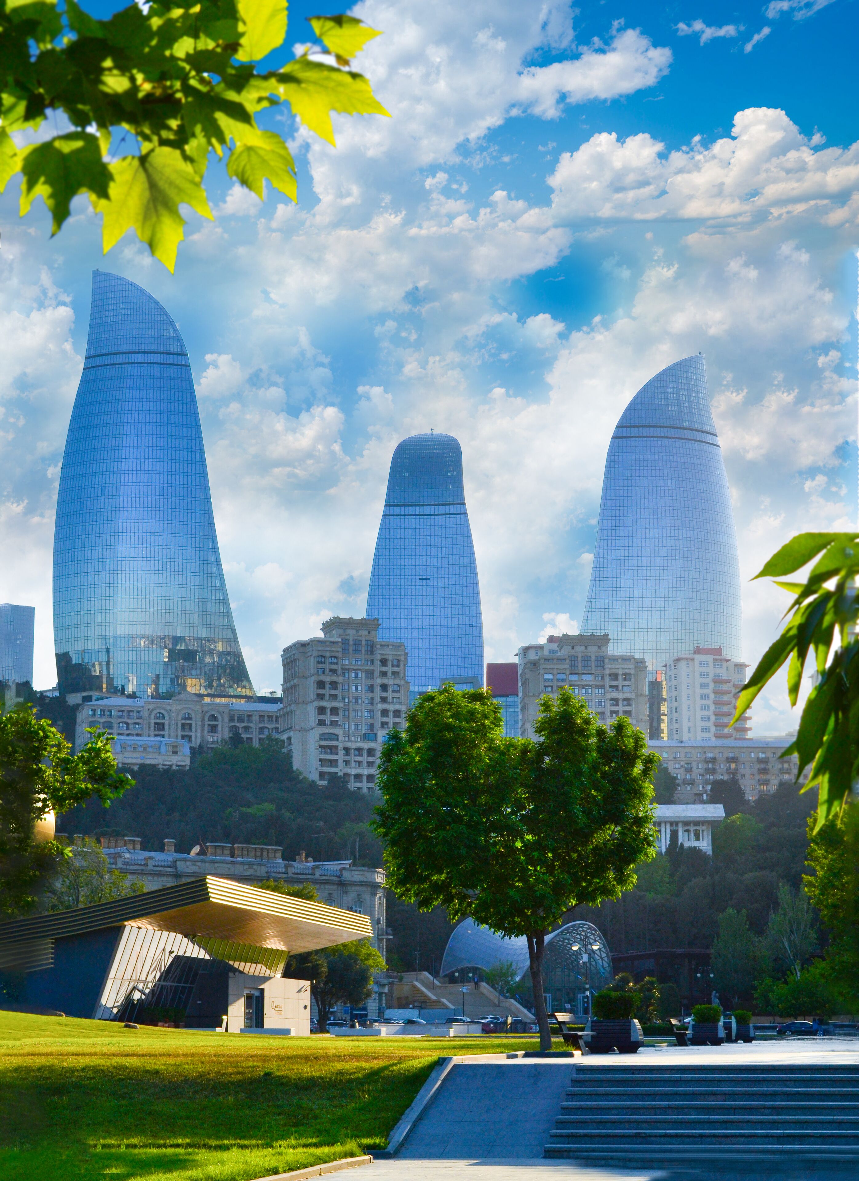 A modern building complex with three prominent skyscrapers, surrounded by greenery and a well-maintained park area.