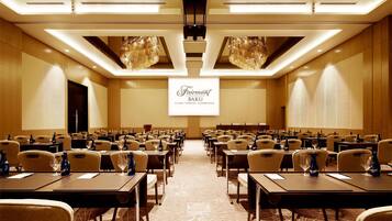 Een vergaderzaal met rijen tafels en stoelen, een groot scherm waarop 'Fairmont Baku Flame Towers, Azerbaijan' staat, en een moderne kroonluchter.