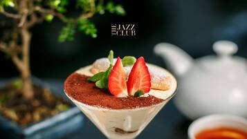Een dessert in een martini-glas met aardbeien en cacaopoeder, een theepot, en aardbeien op een tafel.