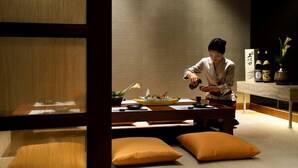 Une pièce de style japonais traditionnel, avec un sol recouvert de tatamis, une petite table basse et une personne qui sert les plats.