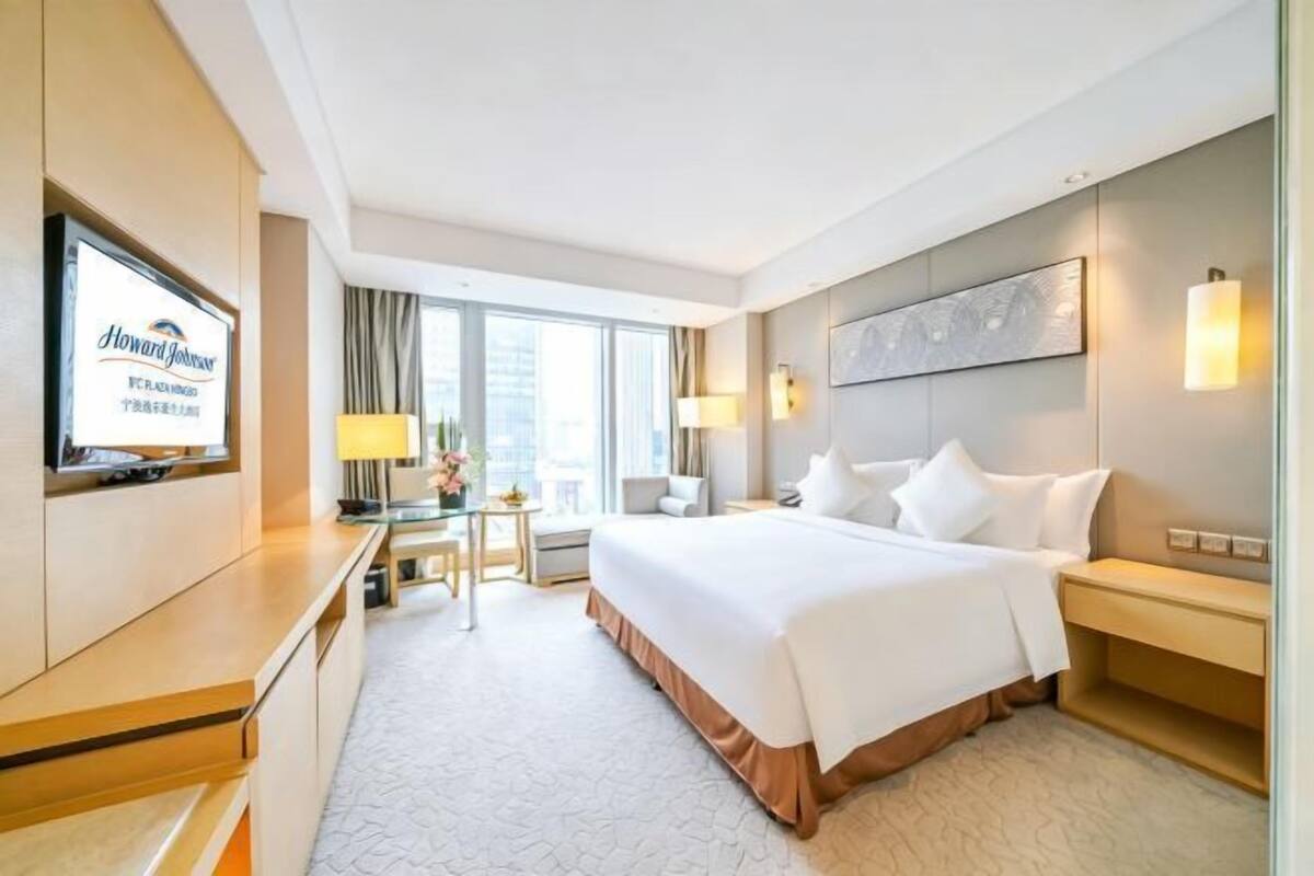 Een hotelkamer met een bed, een bureau, een televisie en een groot raam.