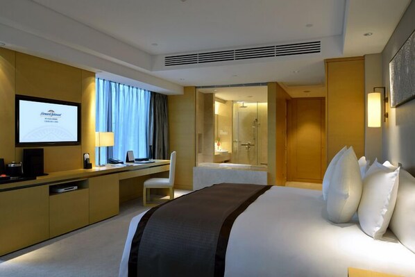 A hotel room with a bed, a desk with a computer, a TV, and a shower area. - Howard Johnson IFC Plaza Ningbo (Ningbo)