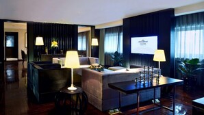 Un hall d’hôtel moderne avec un canapé, des fauteuils, une table basse et un écran de télévision affichant le nom de l’hôtel.
