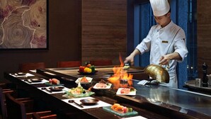 Un chef préparant des plats à une table, avec une variété de mets et un feu.