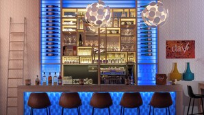 Una zona de bar con mostrador iluminado en azul, varias botellas de vino, copas y una lámpara decorativa.