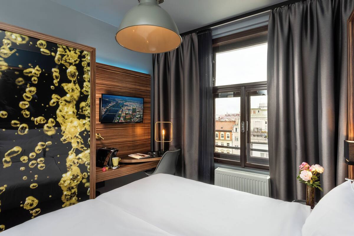 A hotel room with a bed, a desk, a chair, a TV, and a window with curtains.
