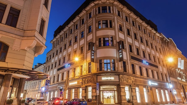Un hotel de varios pisos con un diseño arquitectónico clásico, que destaca por su entrada en esquina e iluminación de señalización.