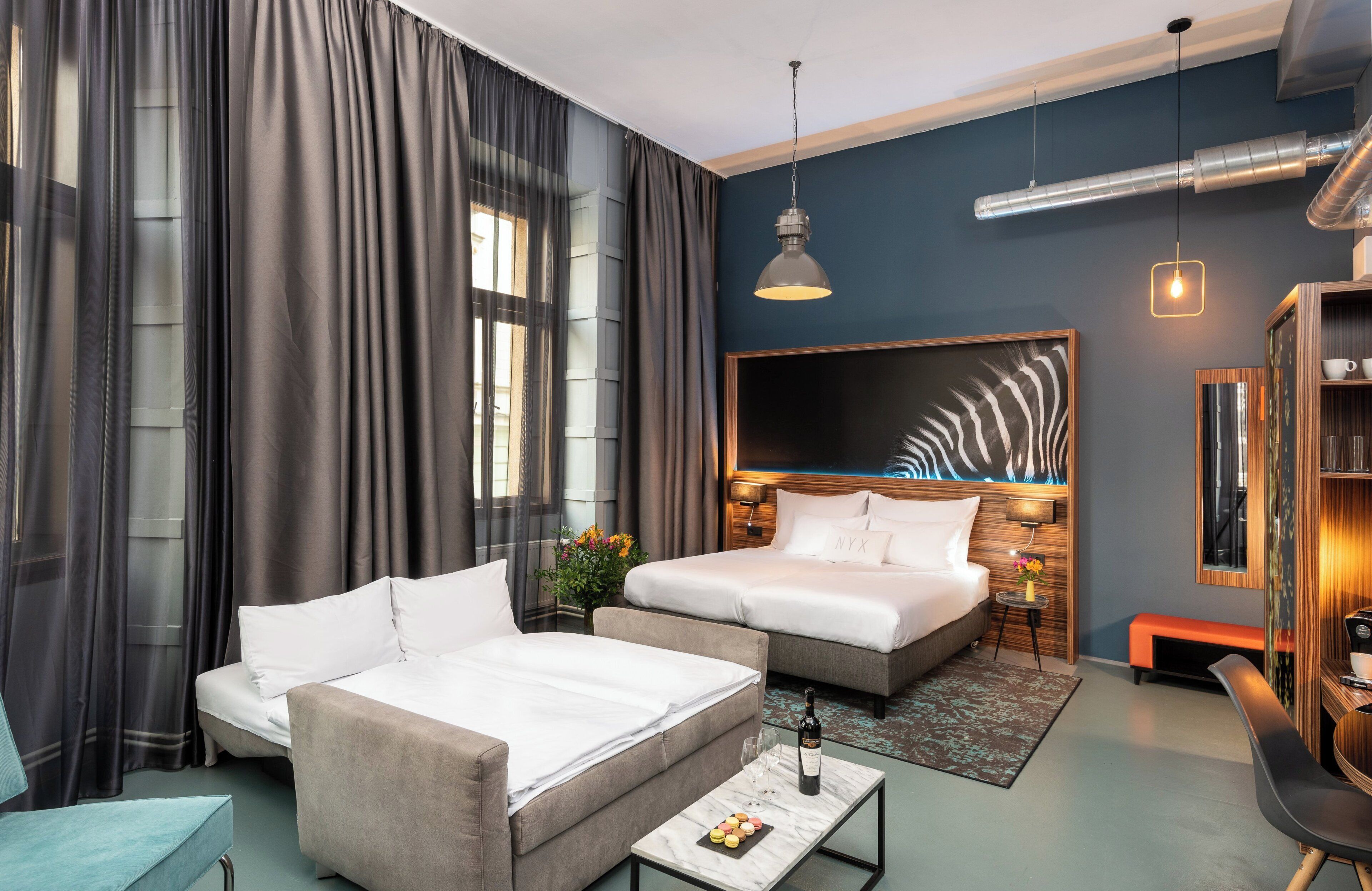 A modern hotel room with a large bed, a sofa, a desk, and a large window with curtains.