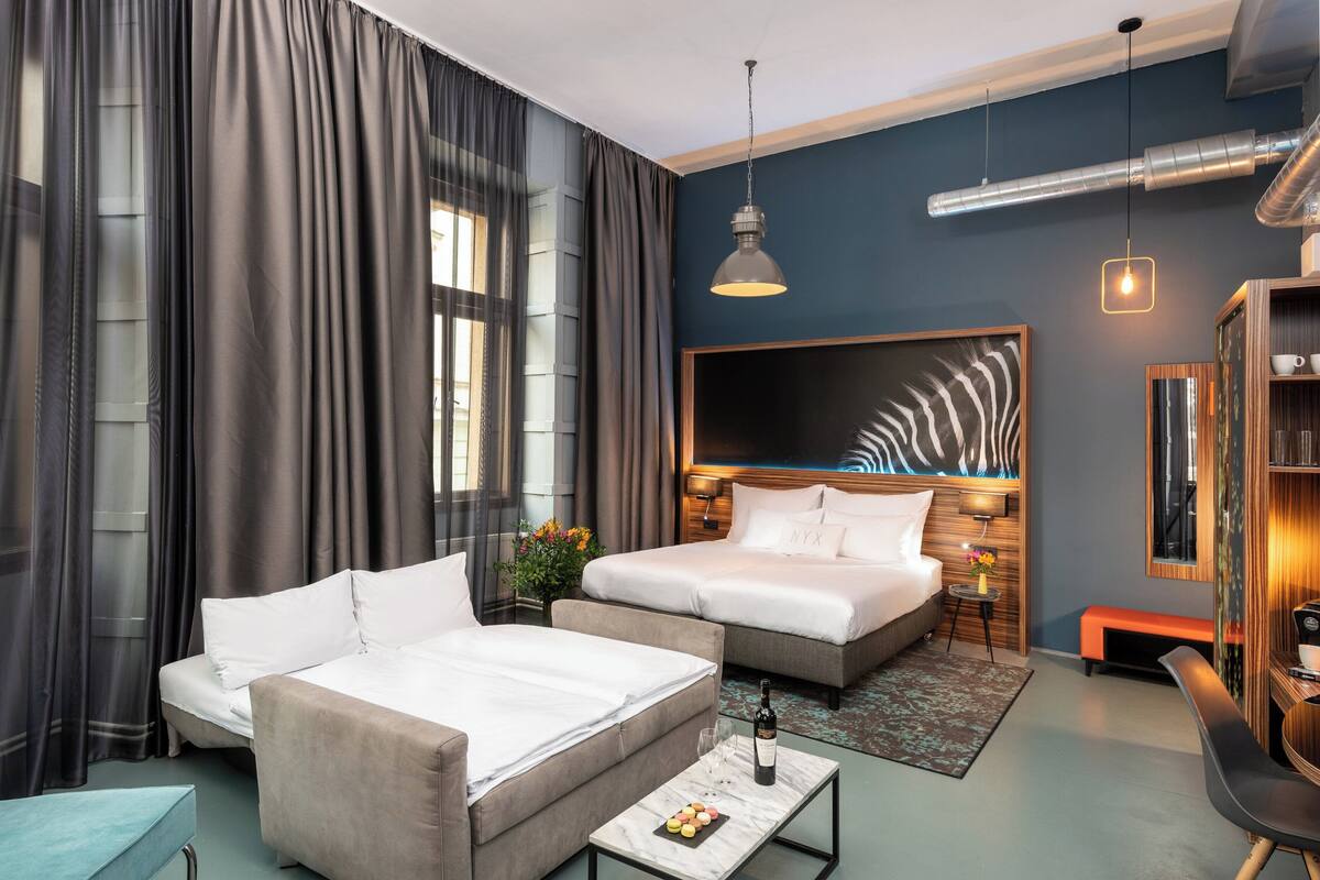 Ein modernes Hotelzimmer mit einem großen Bett, einer Couch, einem Schreibtisch und einem großen Fenster mit Vorhängen.