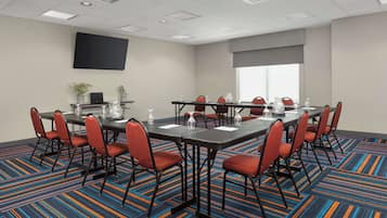 Un salón de conferencias con una amplia mesa, varias sillas y un televisor de pantalla plana en la pared.