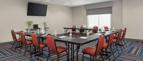 A conference room with a large table, multiple chairs, and a flat-screen TV on the wall.