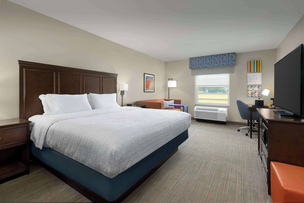 Una habitación de hotel con una cama grande, un escritorio con ordenador, una silla y un televisor.