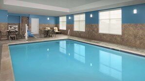 Una piscina interior con suelo de baldosas, una puerta y una zona de estar con sillas y una mesa.