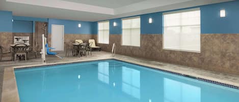 An indoor swimming pool with a tiled floor, a door, and a seating area with chairs and a table.