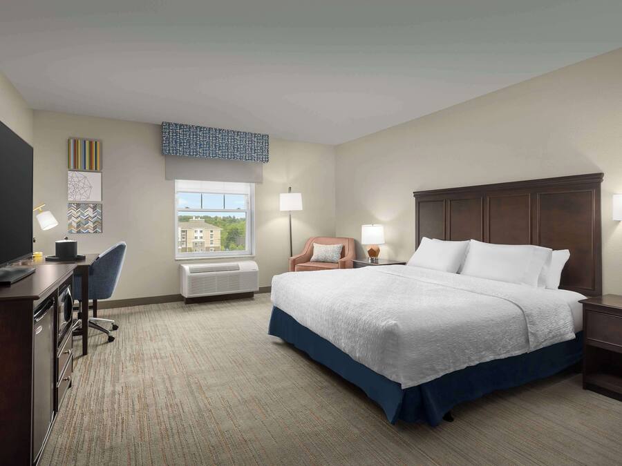 Une chambre d’hôtel avec un lit, un bureau, une chaise et une fenêtre donnant sur un paysage agréable.