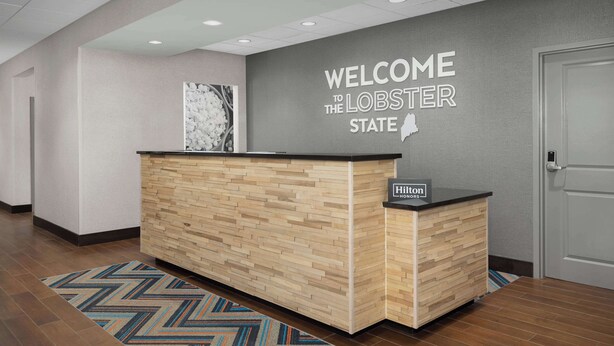 Una mesa de recepción con un cartel que dice "Welcome to the Lobster State", un diseño de paneles de madera y el logotipo de "Hilton".