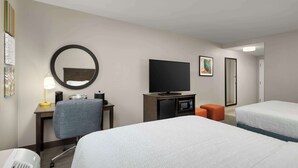 Habitación de hotel con dos camas, un escritorio con silla, un televisor, un microondas y un taburete naranja pequeño.