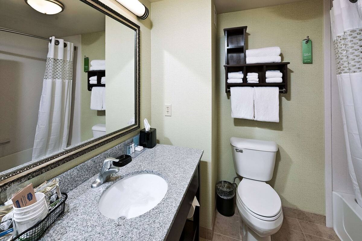 Un baño con lavamanos de granito, inodoro, espejo y toallero.