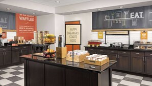Un área de desayuno con un cartel que dice "HAPPY BREAKFAST STARTS HERE" y un cartel promocionando gofres.