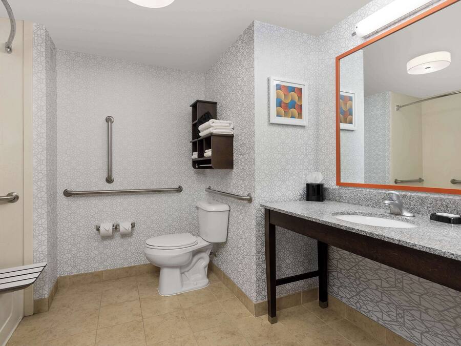 A bathroom with a toilet, handrails, a sink, and a mirror.
