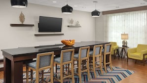 Un comedor moderno con una mesa larga, varias sillas, un televisor y decoración en las paredes.