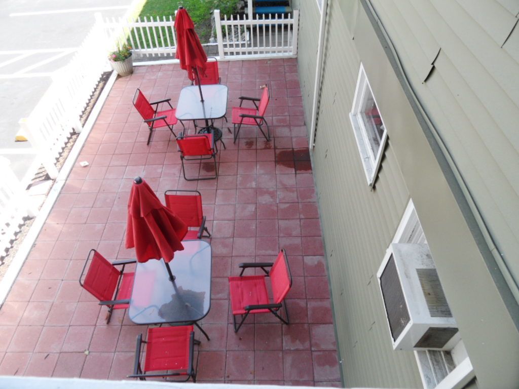 A patio with red chairs and tables, a white fence, and a building with windows and an air conditioning unit.
