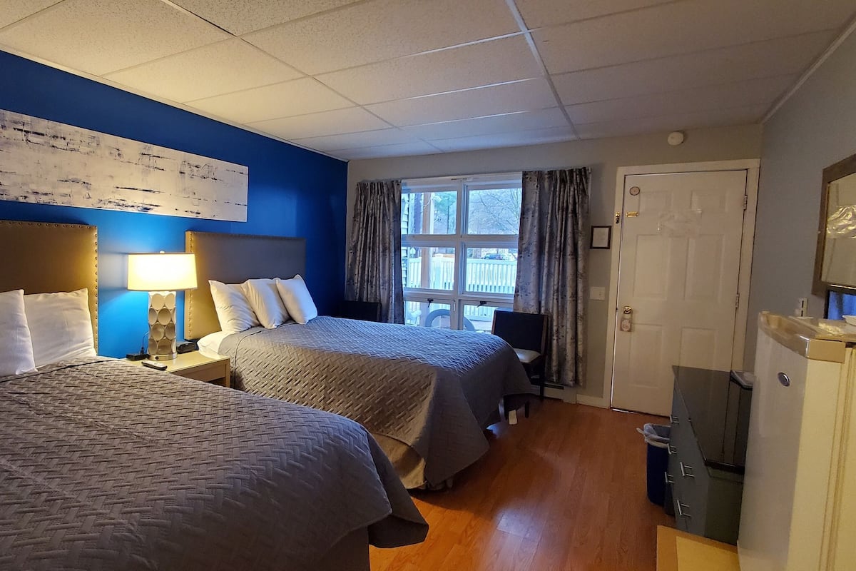 A hotel room with two beds, a large abstract painting on the wall, a window with curtains, and a refrigerator.