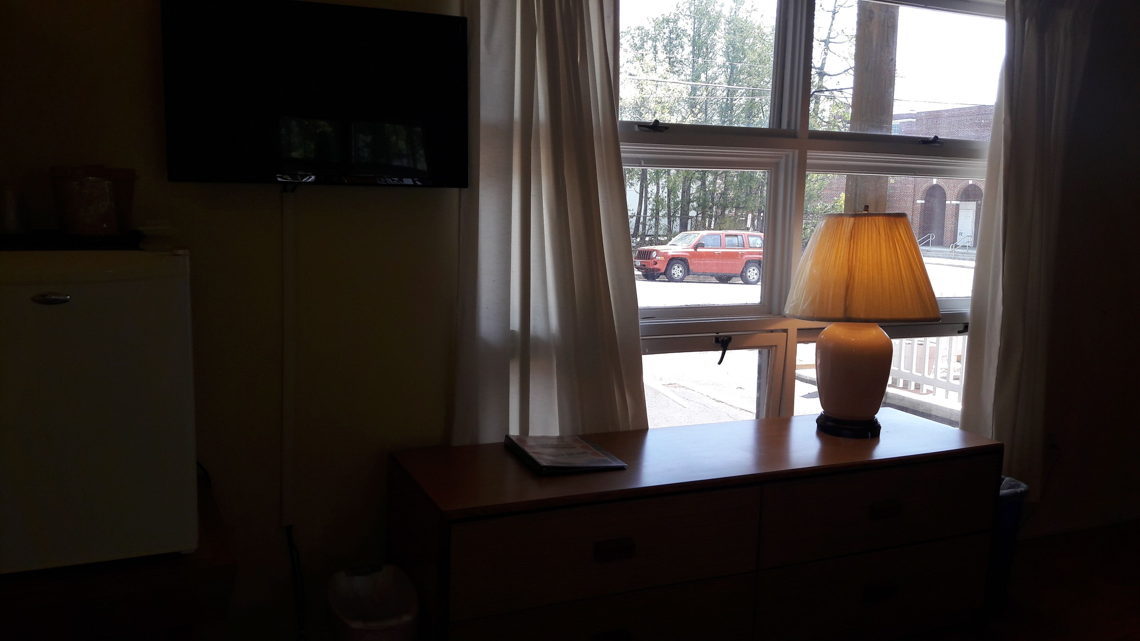 Una habitación con ventana, lámpara, televisor de pantalla plana y una pequeña mesa.