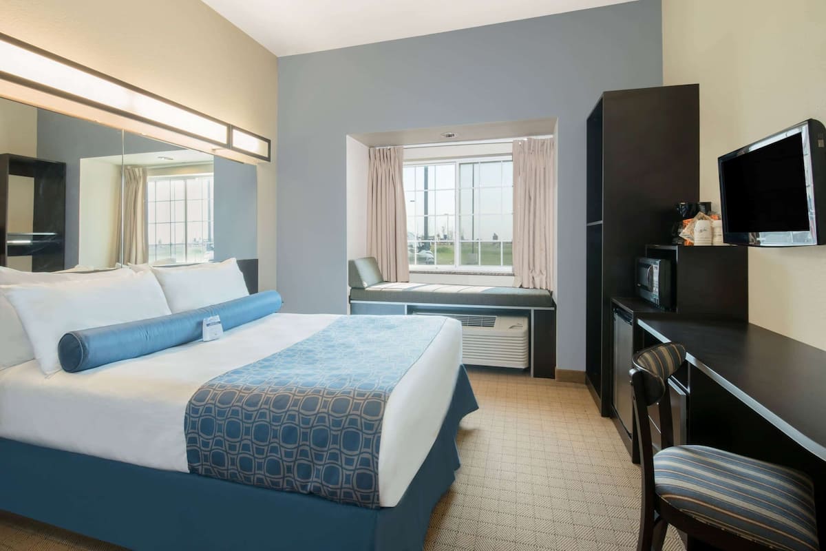 Una habitación de hotel con cama, escritorio, silla, televisión y ventana con cortinas.
