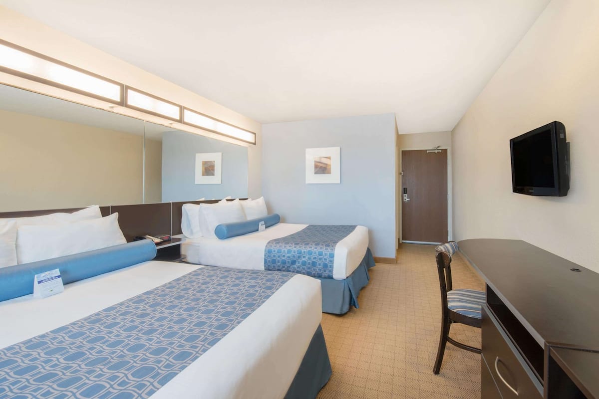 Habitación de hotel con dos camas, un escritorio, una silla, un televisor y una puerta.