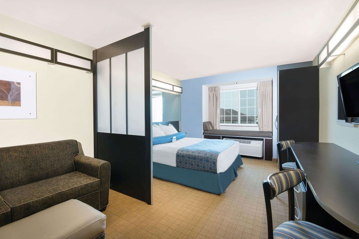 Habitación de hotel con cama, sofá, mesa de comedor y televisor.