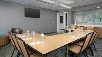 Un salón de conferencias con una mesa larga, sillas, botellas de agua y una puerta.
