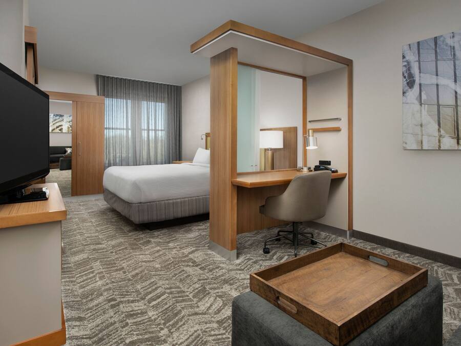 A hotel room with a bed, a desk, a television, a chair, and a tray table.