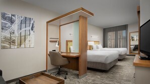 Habitació d'hotel amb escriptori, dos llits, una cadira, televisió i obra d'art a la paret.