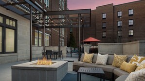 Un patio al aire libre con un hogar para fuego, asientos y una pérgola con luces colgantes.