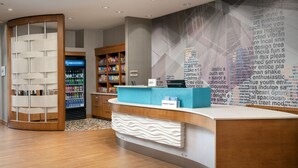 Zona de recepció d'hotel amb un disseny modern, que inclou un taulell de recepció corbat, una paret amb un núvol de paraules i una màquina de begudes d'auto-servei.