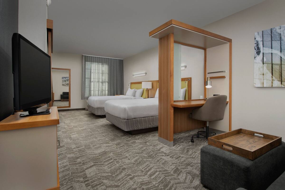 Hotelkamer met twee bedden, een bureau, een stoel, een televisie en een groot raam met gordijnen.