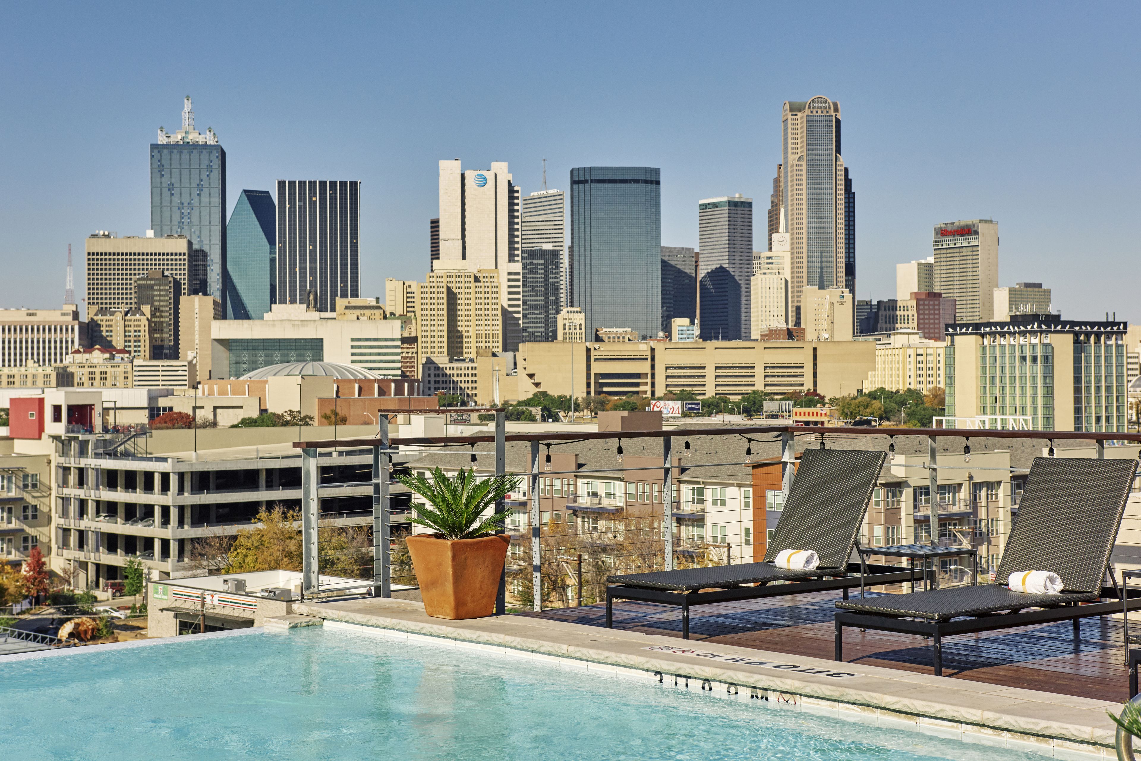 A rooftop pool with lounge chairs and a city skyline in the background.