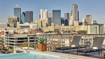 A rooftop pool with lounge chairs and a city skyline in the background.